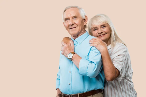 Alegre jubilado mujer abrazando mayor marido aislado en beige - foto de stock