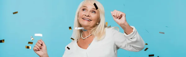 Панорамний знімок щасливої пенсіонерки, дивлячись на падаючу конфетті на синьому — стокове фото