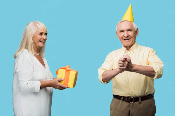 Aposentado mulher dando caixa de presente amarelo para o marido sênior feliz isolado no azul — Fotografia de Stock