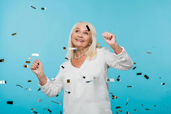 Mujer jubilada feliz mirando caer confeti en azul - foto de stock