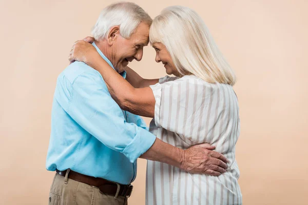 Fröhliches Rentnerehepaar, das sich beim Umarmen vereinzelt auf beige schaut — Stockfoto