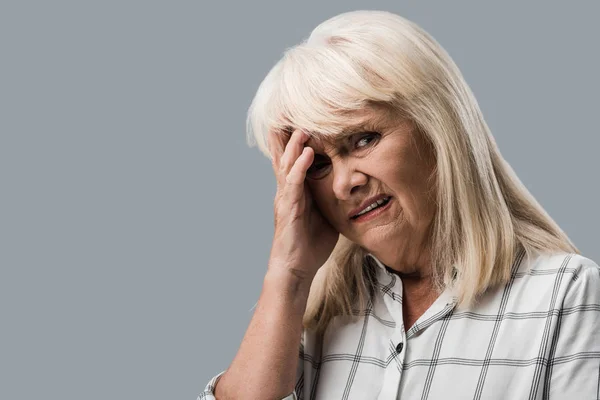 Tired and upset retired woman touching head and looking at camera isolated on grey — Stock Photo