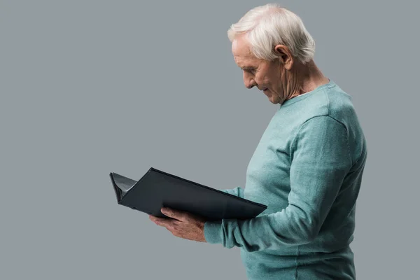 Glücklicher Rentner mit grauen Haaren schaut auf Fotoalbum isoliert auf grau — Stockfoto