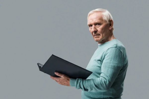 Засмучений чоловік на пенсії з сірим волоссям тримає фотоальбом ізольовано на сірому — стокове фото