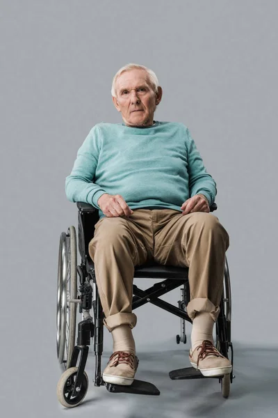 Sad senior man sitting in wheelchair and looking at camera on grey — Stock Photo
