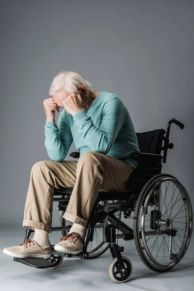 Retired man sitting in wheelchair and covering face on grey — Stock Photo