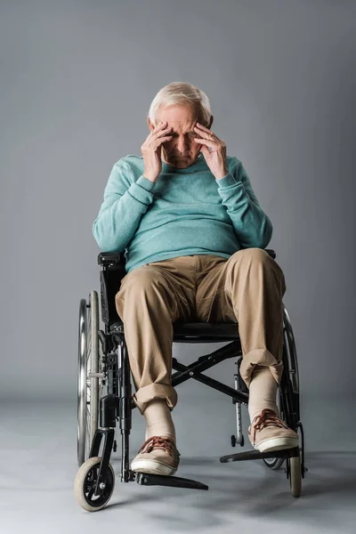 Sconvolto uomo in pensione seduto in sedia a rotelle e toccare la testa sul grigio — Foto stock