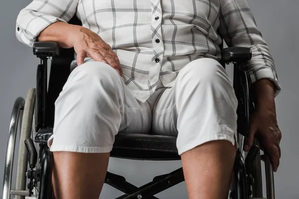 Обрезанный вид инвалида пенсионерки, сидящей в инвалидной коляске и трогательного колена, изолированного на сером — стоковое фото