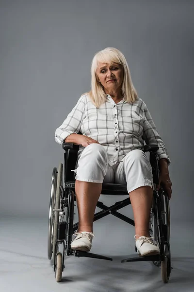 Upset and disabled retired woman sitting in wheelchair on grey — Stock Photo