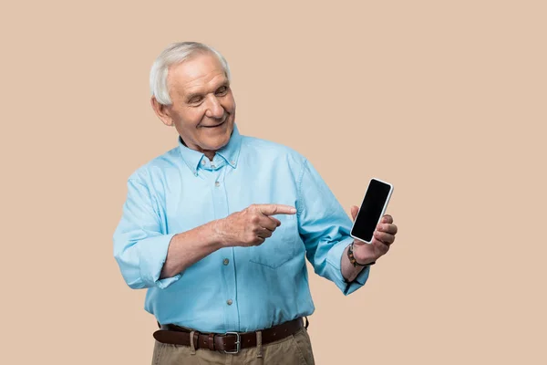 Happy retired man with grey hair pointing with finger at smartphone with blank screen isolated on beige — Stock Photo
