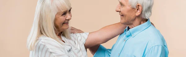 Panoramic shot of senior woman smiling while looking at pensioner isolated on beige — Stock Photo