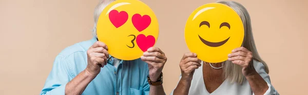 KYIV, UKRAINE - 14 JUIN 2019 : plan panoramique d'un couple de personnes âgées couvrant des visages avec des sourires heureux jaunes isolés sur du beige — Photo de stock