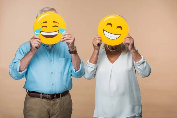 KYIV, UCRANIA - 14 DE JUNIO DE 2019: pareja mayor cubriendo caras con emoticonos amarillos felices aislados en beige - foto de stock