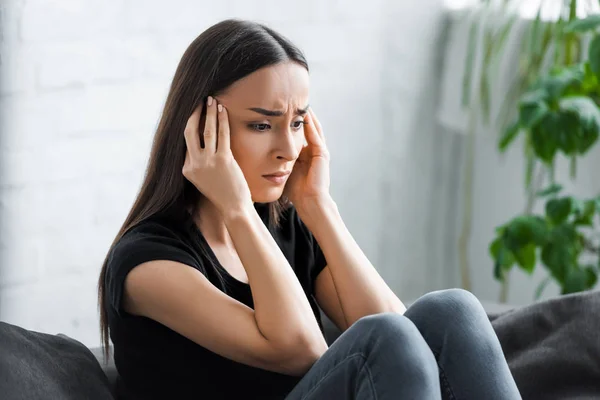 Depressed young woman holding hands near head while sitting on sofa at home — Stock Photo