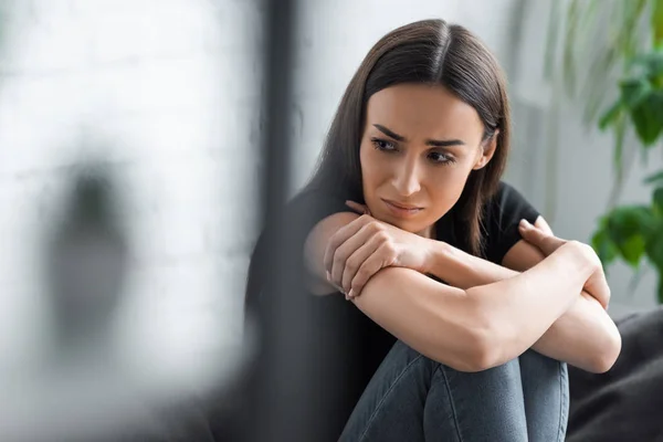 Вибірковий фокус плачу молодої жінки, яка страждає від депресії, сидячи з схрещеними руками і дивлячись — стокове фото