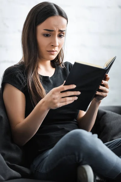 Upset young woman suffering from dementia and looking at notebook while sitting on couch at home — Stock Photo