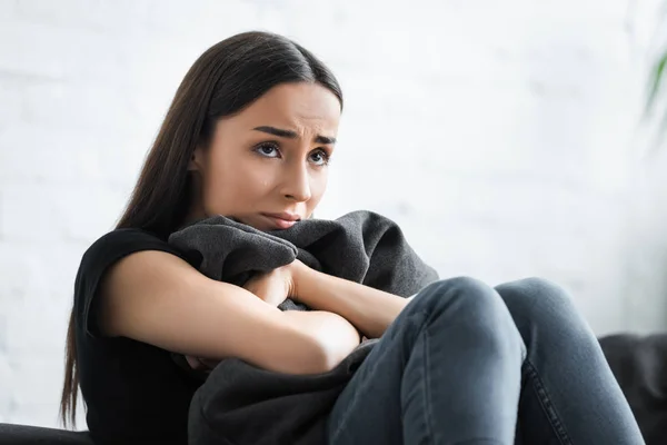 Depresso giovane donna abbracciando cuscino e guardando lontano mentre seduto sul divano a casa — Foto stock