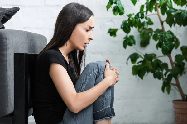 Young woman sitting on floor at home and suffering from panic attack — Stock Photo