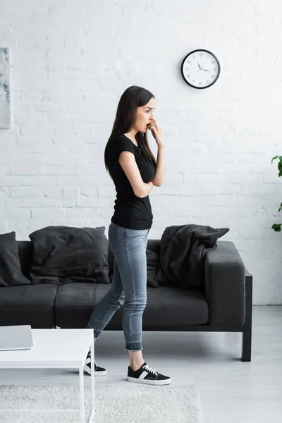 Mujer joven molesta sosteniendo la mano cerca de la cara y mirando hacia otro lado mientras sufre de depresión en casa - foto de stock