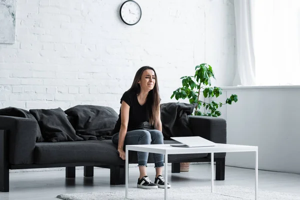 Crying woman sitting on sofa at home while suffering from depression — Stock Photo