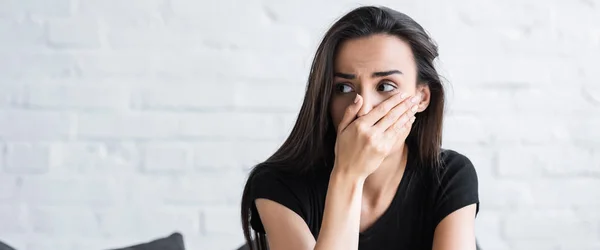 Femme effrayée tenant la main sur le visage et regardant loin tout en souffrant d'une attaque de panique à la maison — Photo de stock