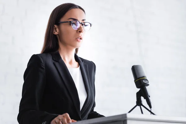 Serio joven profesor de gafas y ropa formal de pie en el podio tribuna - foto de stock