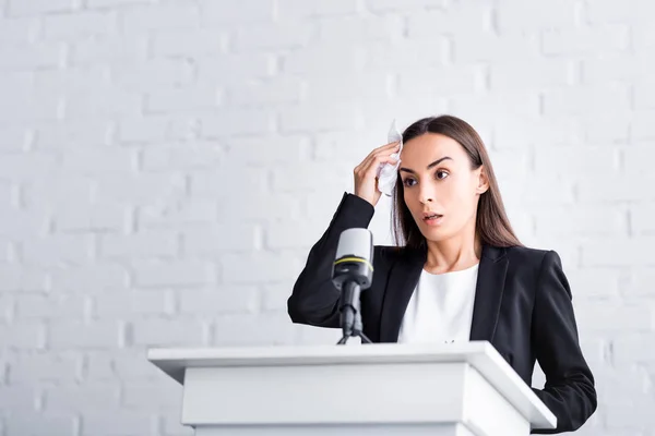 Worried lecturer, suffering from glossophobia, holding napkin near forehead while standing on podium tribune — Stock Photo