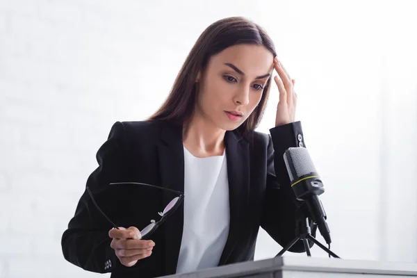 Thoughtful, nervous lecturer standing on podium tribune and holding hand near head — Stock Photo