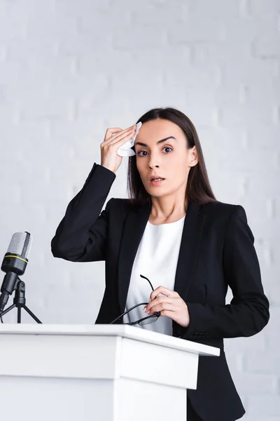 Nervous lecturer suffering from fear of public speaking holding napkin and looking at camera while standing on podium tribune — Stock Photo