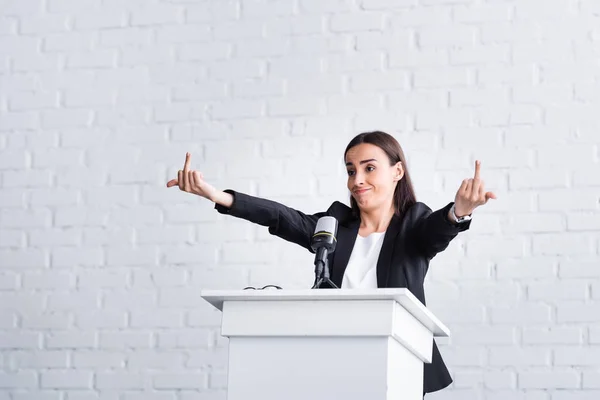 Раздраженный преподаватель показывает средний палец, стоя на трибуне на трибуне в конференц-зале — стоковое фото