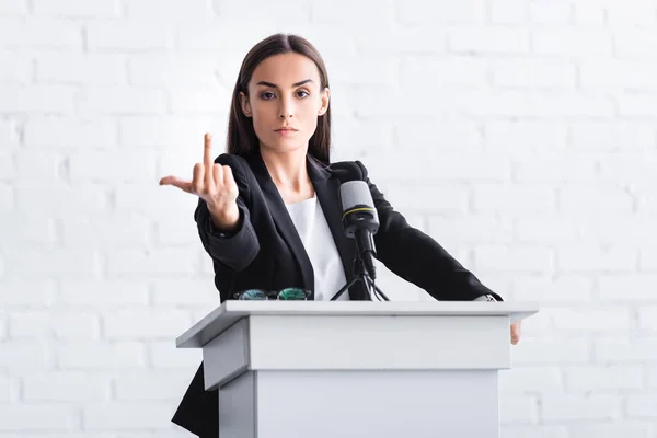 Irritated lecturer standing at podium tribune while showing middle finger at camera — Stock Photo