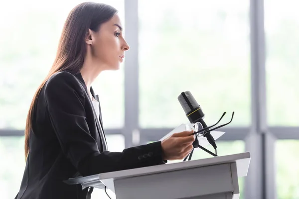 Serious lecturer holding glasses while standing on podium tribune in conference hall — Stock Photo