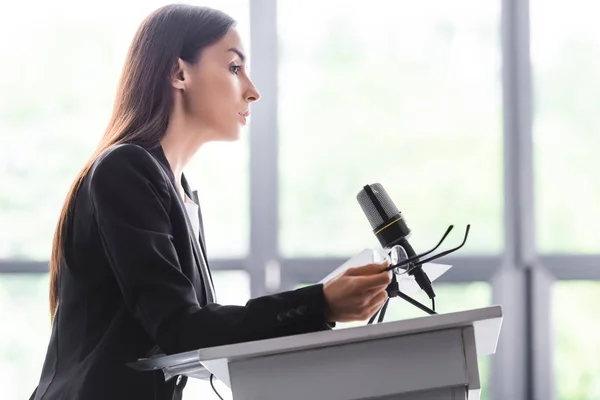 Serio docente che tiene gli occhiali mentre è in piedi sul tribuna del podio nella sala conferenze — Foto stock