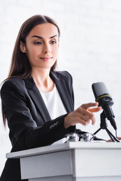 Улыбающийся преподаватель трогает микрофон, стоя на трибуне в конференц-зале — стоковое фото