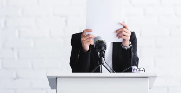 Jeune conférencier, souffrant de peur de parler en public, debout sur le podium tribune et se cachant face derrière la feuille de papier — Photo de stock