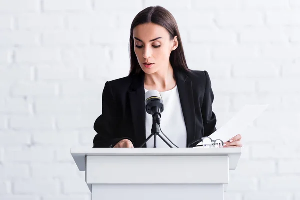 Attractive young lecturer standing on podium tribune and looking at papers — Stock Photo