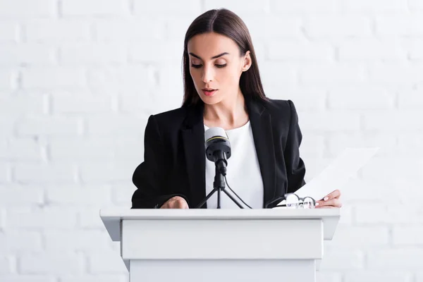 Attraktive junge Dozentin, die auf der Podiumstribüne steht und Papiere betrachtet — Stockfoto