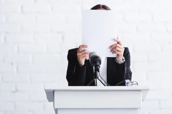 Scared lecturer suffering from logophobia and hiding face behind paper while standing at podium tribune — Stock Photo