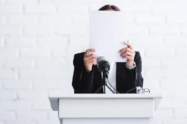 Verängstigter Dozent, der an Logophobie leidet und sein Gesicht hinter Papier versteckt, während er am Podium steht — Stockfoto