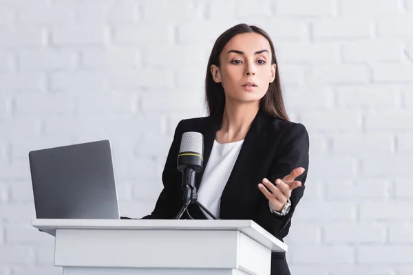 Attractive serious lecturer gesturing while speaking from podium tribune — Stock Photo