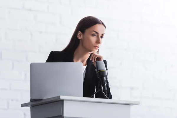 Pensive lecturer standing on podium tribune near microphone and laptop — Stock Photo