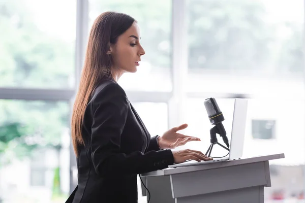 Attractive, confident lecturer gesturing while speaking from podium tribune — Stock Photo