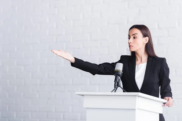 Attractive, confident lecturer pointing with hand while standing on podium tribune — Stock Photo