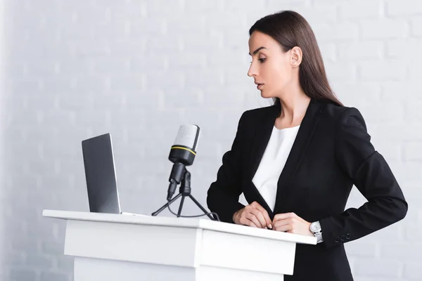 Conférencier sérieux debout sur le podium tribune près de microphone et ordinateur portable — Photo de stock