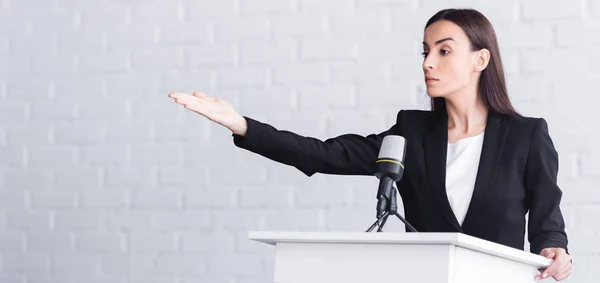 Panoramische Aufnahme eines schönen, ernsten Vortragenden, der mit der Hand zeigt, während er auf der Tribüne steht — Stockfoto