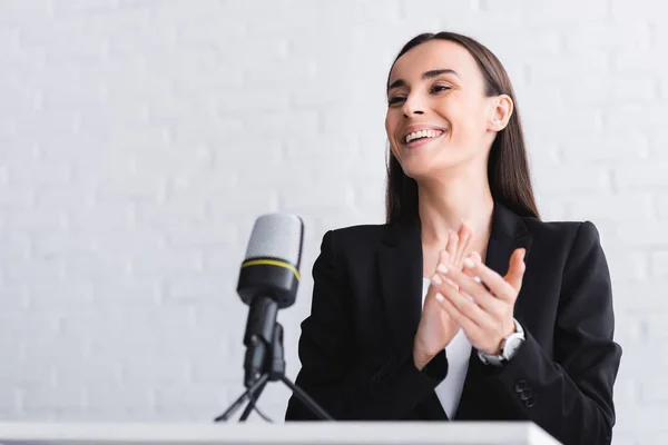 Beautiful, happy lecturer clapping hands while standing on podium tribune — Stock Photo