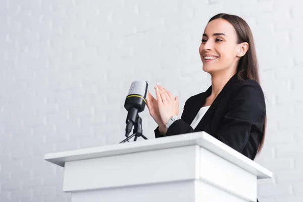 Happy speaker clapping hands while standing on podium tribune in conference hall — Stock Photo