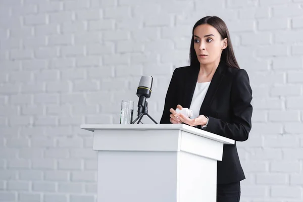Pretty lecturer, suffering from glossophobia, standing on podium tribune and holding container with pills — Stock Photo