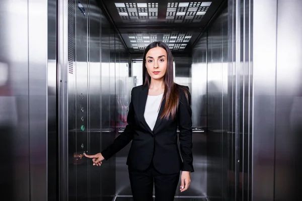 Приваблива, впевнена бізнес-леді натискає кнопку в ліфті і дивиться на камеру — стокове фото