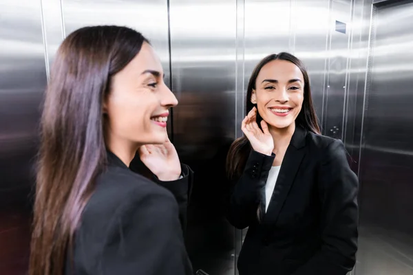 Atractiva, mujer de negocios feliz en ascensor sonriendo y saludando de la mano - foto de stock